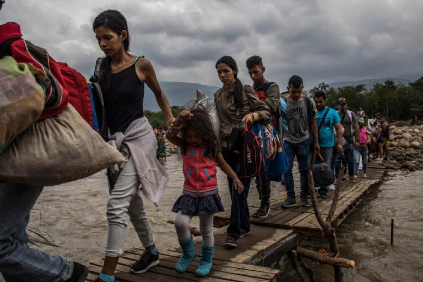 Refugiados cruzam ponte sobre rio.
